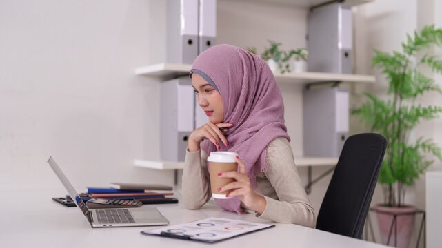 Asian Muslim businesswoman adult working laptop computer analyzing data focused expression office space entrepreneurial endeavors remote work digital transformation business growth
