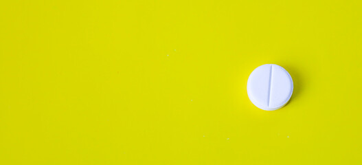 A large white round pill with a line in the middle, placed on a bright yellow background, creates a...