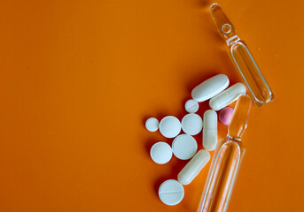 Medical ampoules and various pills, arranged on an orange background, create a visualization of...