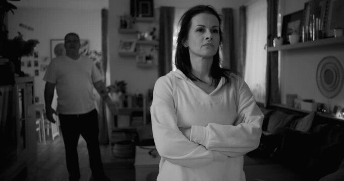 Close-up of woman with stern expression during heated argument, man blurred in background gesturing angrily, capturing emotional tension and unresolved conflict