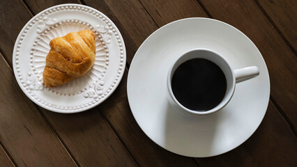 Top view of a cup of coffee and a croissant on a dark background.