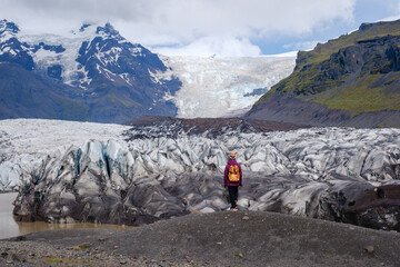 A traveler stands in awe at Svinafellsjokull Glacier, surrounded by rugged terrain and breathtaking...