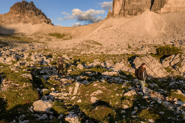 Hikers exploring rocky trails at the foot of Tre Cime di Lavaredo during golden hour, Dolomites,...