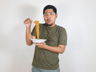 Handsome Asian man holding noodles with a fork while showing a shocked and worried expression. Eating lunch concept. Isolated white background.