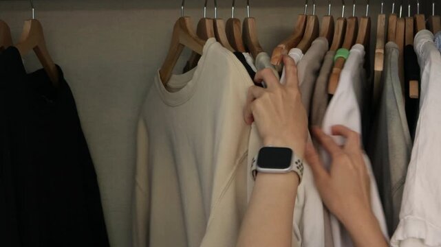 Choosing clothes from wardrobe, hands sorting minimalist outfits