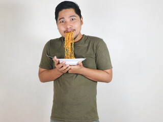 Handsome Asian man enjoying noodles, with the noodles still in his mouth. Eating lunch concept....