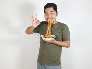 Handsome Asian man enjoying noodles, with the noodles still in his mouth, and giving an okay sign....