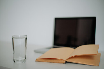 Workspace with glass of water, laptop, and open book, neutral tones and clarity.
