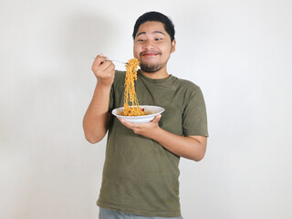 Handsome Asian man enjoying noodles with a fork with an expression of being very tempted by the...