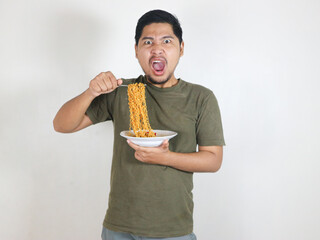 Handsome Asian man holding noodles with a fork while angry and shouting. Eating lunch concept. Isolated white background