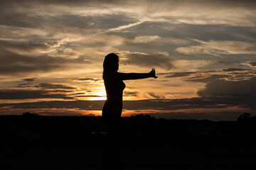 Silhouette of a plump young woman warming up before exercising for better health during sunset.