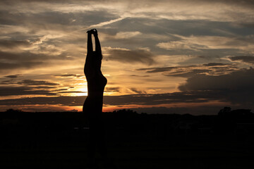 Silhouette of a plump young woman warming up before exercising for better health during sunset.