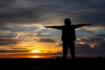 Silhouette of a plump young woman warming up before exercising for better health during sunset.