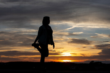 Silhouette of a plump young woman warming up before exercising for better health during sunset.