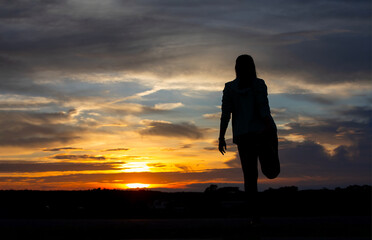 Silhouette of a plump young woman warming up before exercising for better health during sunset.