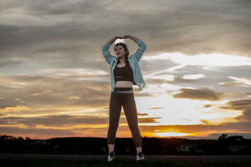 A plump young woman warms up before exercising for better health during sunset.
