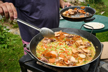 Chef preparing seafood paella outdoors in large pan