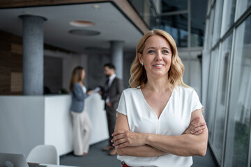 Confident businesswoman smiling with folded arms in modern office lobby