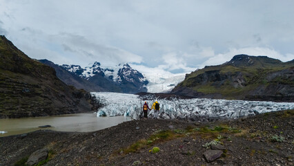 Adventurers stand at the base of Svinafellsjokull Glacier, marveling at its stunning icy formations...