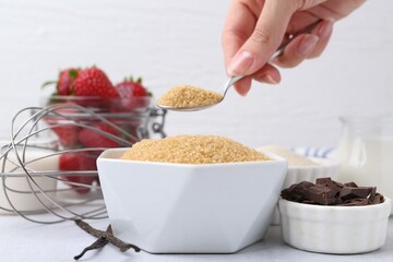 Making tasty panna cotta. Woman taking sugar with spoon at white table, closeup