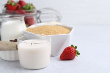 Different ingredients for panna cotta. Milk, sugar, vanilla and strawberries on white table, closeup