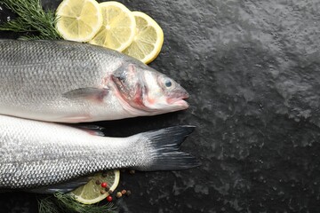 Fresh raw seabass fish with spices on black table, flat lay and space for text. Seafood delicacies