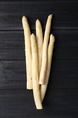 Raw white asparagus spears on black wooden table, top view