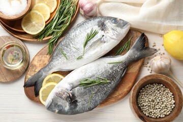 Fresh raw dorado fish, lemon slices, rosemary and spices on white wooden table, flat lay. Organic seafood