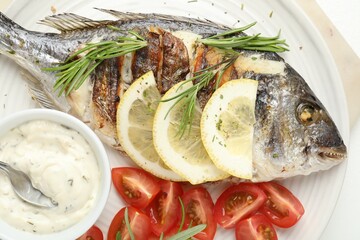 Tasty roasted dorado fish with sauce, tomatoes and lemon on white table, top view. Homemade seafood dish
