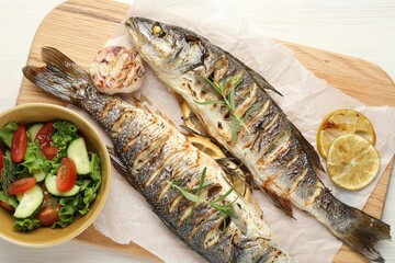 Tasty roasted seabass fish served with salad and lemon on white wooden table, top view. Homemade seafood dish