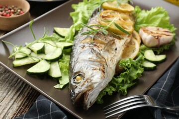 Tasty roasted seabass fish served with vegetables and lemon on wooden table, closeup. Homemade seafood dish