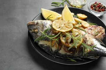Tasty roasted dorado fish with potatoes, rosemary and lemon on grey table, closeup. Homemade seafood dish