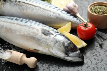 Fresh raw mackerels and spices on black table, closeup. Seafood delicacies