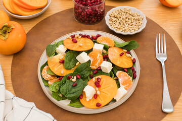 Winter salad. Fresh persimmon and pomegranate spinach salad with feta and pine nuts. Copy space