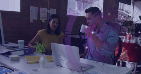 Collaborating colleagues reviewing data on laptop at office, with coffee mug and papers