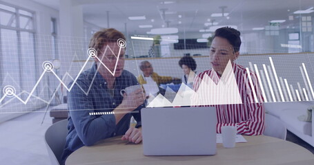 Two colleagues in denim shirt, striped blouse collaborating in open-plan office with silver laptop