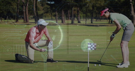 Kneeling man marking golf ball and woman lining up putt on putting green, wearing polo shirts