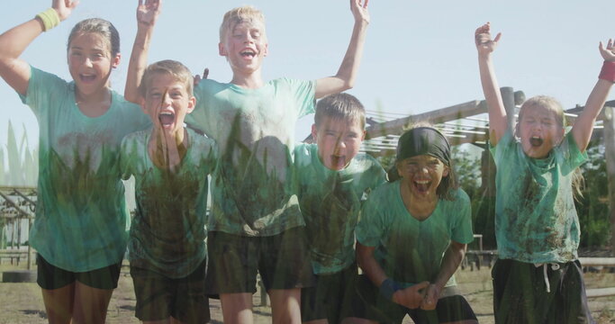 Cheering six kids covered in mud on course at camp, with headbands wristbands beams framework