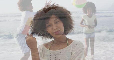 Standing woman wearing tunic with green bikini straps at sandy shoreline, boy tossing beach ball
