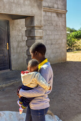 Africa village, single young african mother woman with the back, walking holding the child in her...