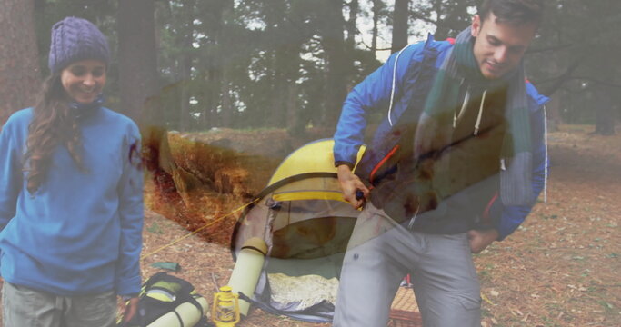 Couple in hiking gear pitching yellow dome tent on pine forest floor, with backpack and lantern - Powered by Adobe