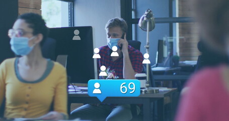 Masked man wearing checkered shirt speaking on mobile in office with monitors notification overlay