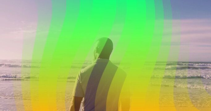 Staring African American man wearing light shirt at waves on sandy beach, with green yellow overlay