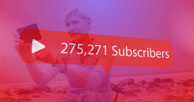 Recording middle-aged woman holding smartphone at rocky shoreline, with subscriber overlay graphic - Powered by Adobe