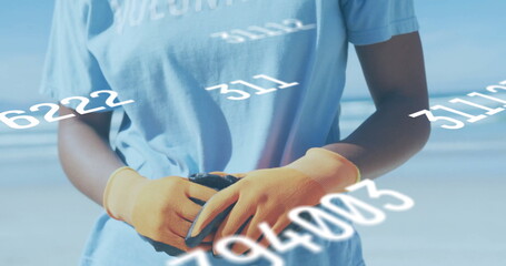 Picking up debris volunteer wearing blue shirt and orange gloves on shoreline, with data overlays