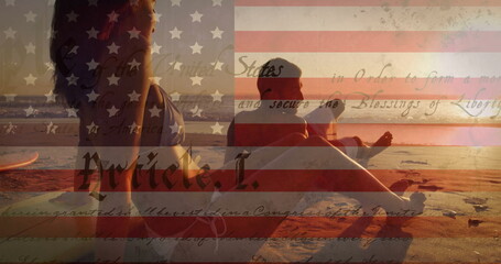 Relaxing couple in swimwear on sandy shore at sunset, with surfboard American flag script overlay