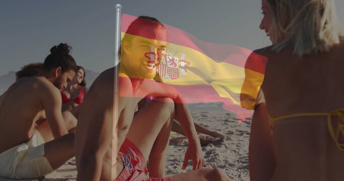 Chatting man wearing red swim trunks talking with friends on sandy beach, with Spanish flag overlay