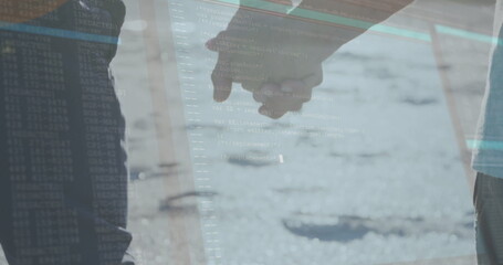 Walking couple wearing jeans and light pants holding joined hands on sunlit road, with code overlay