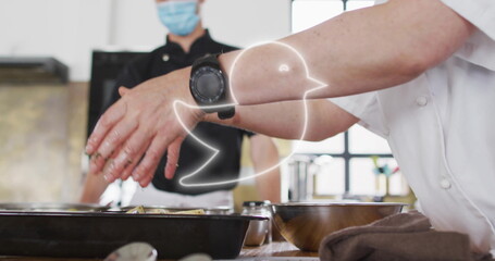 Sprinkling seasoning with chef's hands over metal trays in commercial kitchen, with smartwatch