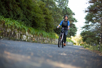 Male wearing bike helmet and backpack riding bicycle along rural road beside stone wall